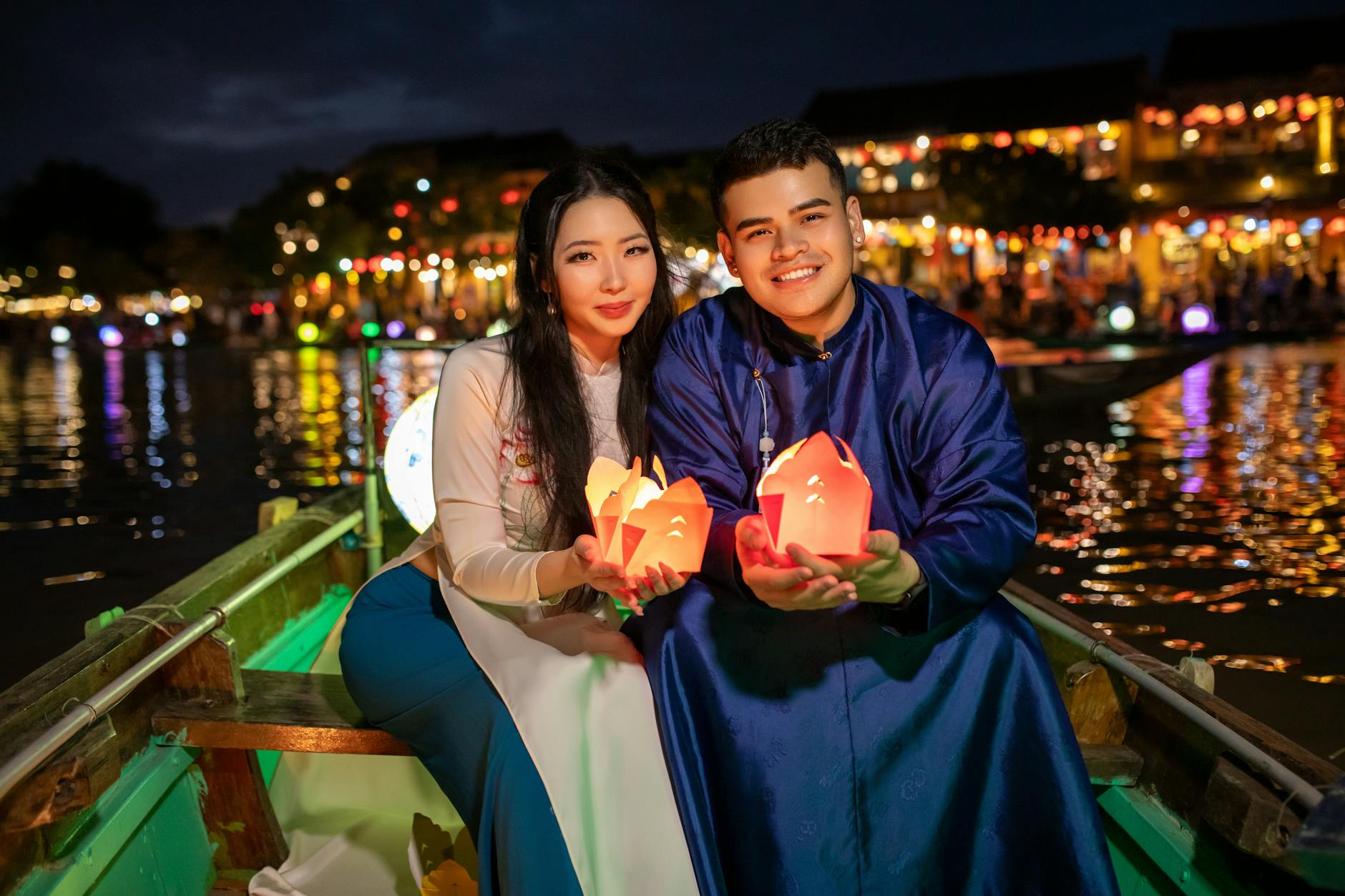 Silhouetted couple floating a krathong together under a sky filled with rising lanterns at dusk