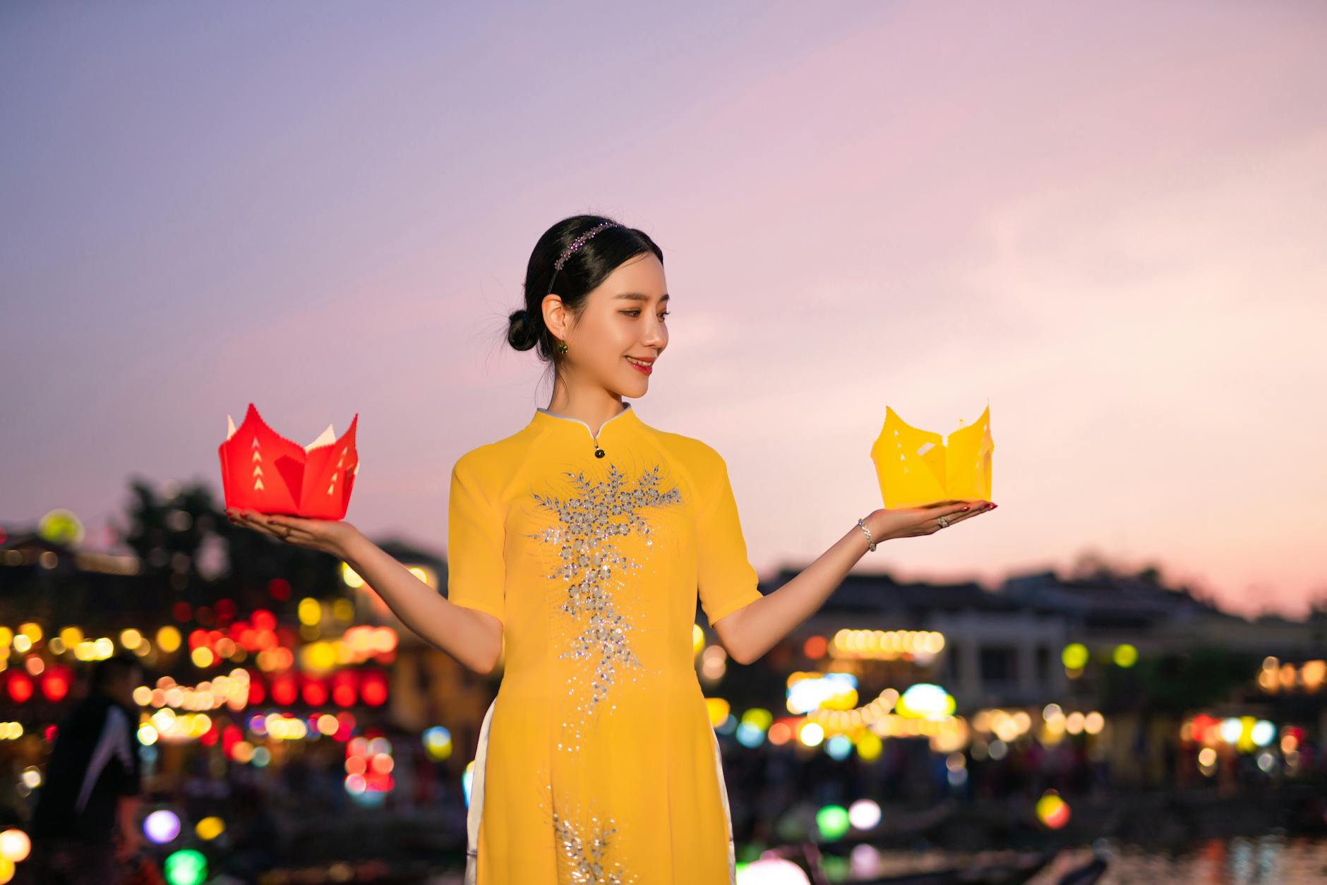 A sky lantern being carefully lit by two hands before release, with lanterns rising in the background