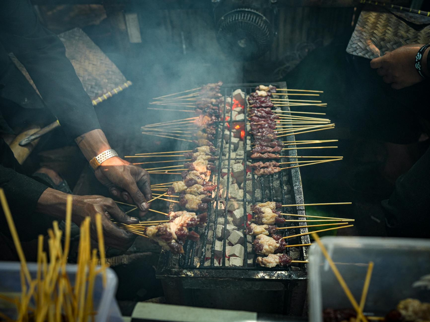 Street food vendor grilling skewers beside a Songkran celebration with water flying everywhere