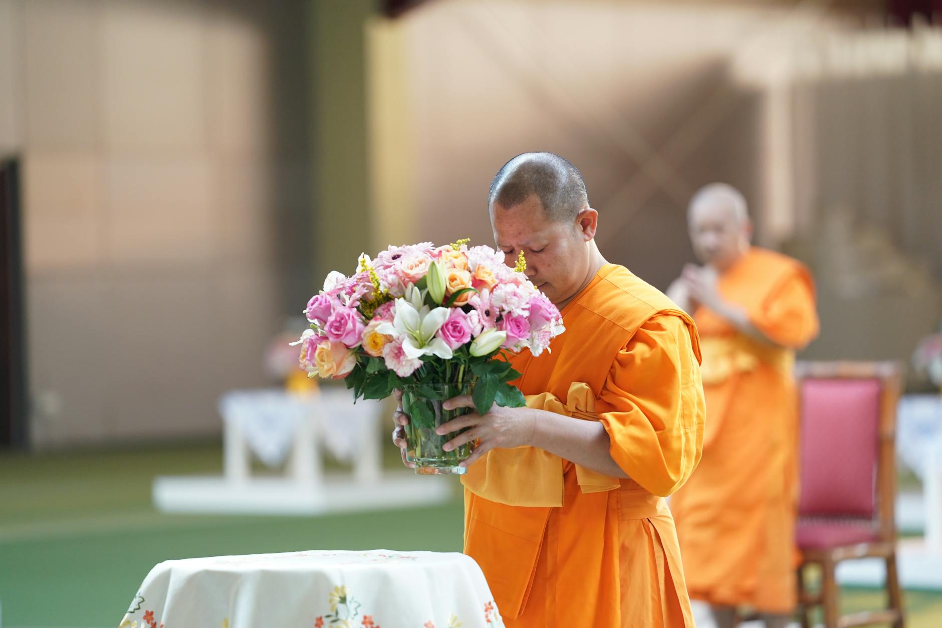 A woman correctly placing an offering onto a receiving cloth held by a male intermediary, with a monk standing at a respectful distance