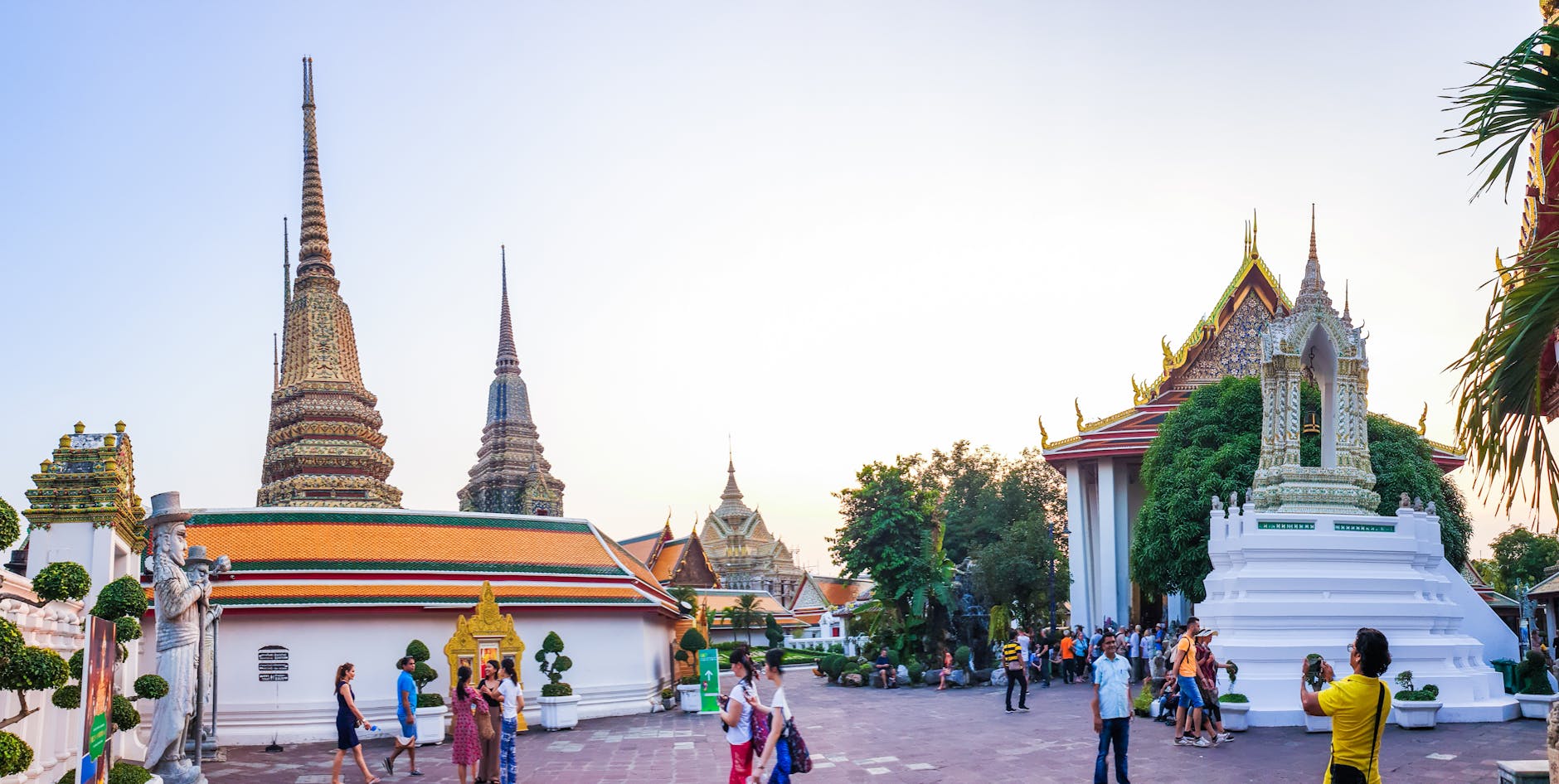 Hundreds of devotees holding lit candles in a clockwise candlelight procession around a golden temple chedi at dusk