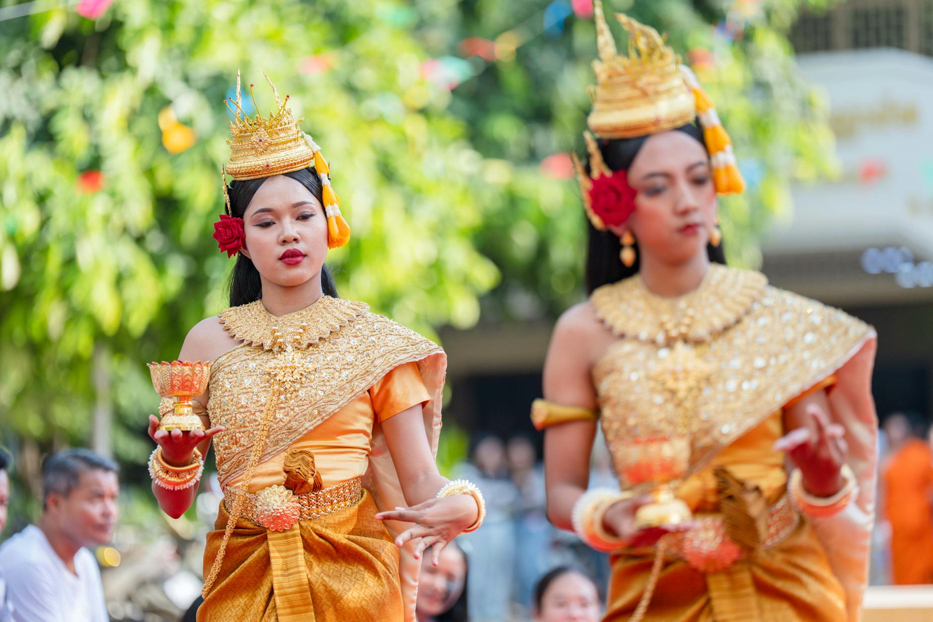 Thai dancers in traditional costumes performing at a festival with golden headdresses and vibrant silk garments